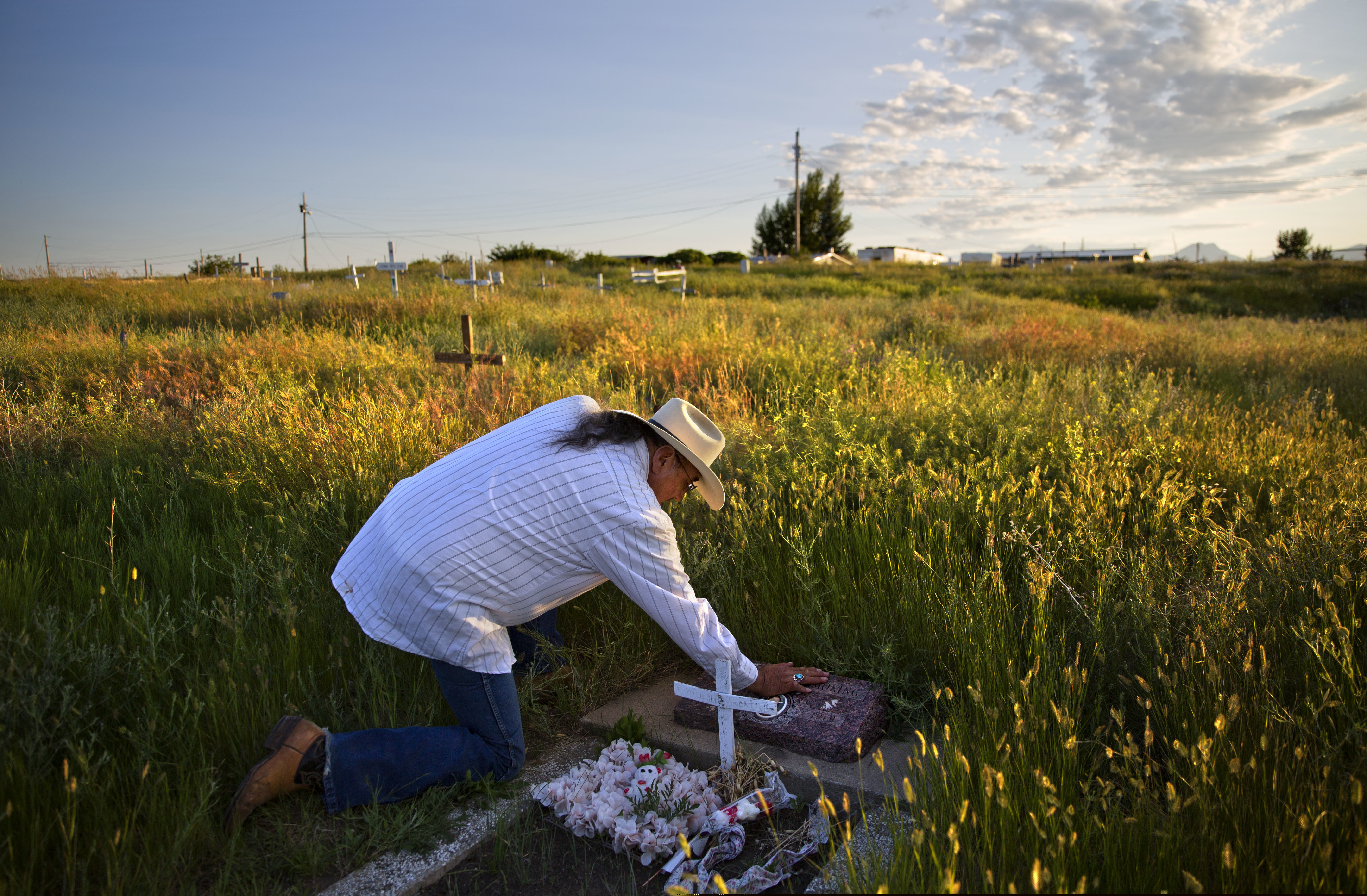 (David Goldman | AP file photo) In this July 14, 2018, file photo, Kenny Still Smoking touches the tombstone of his 7-year-old daughter, Monica, who disappeared from school in 1979 and was found frozen on a mountain, as he visits her grave on the Blackfeet Indian Reservation in Browning, Mont. A study released by a Native American non-profit says numerous police departments in cities nationwide are not adequately identifying or reporting cases of missing and murdered indigenous women.
