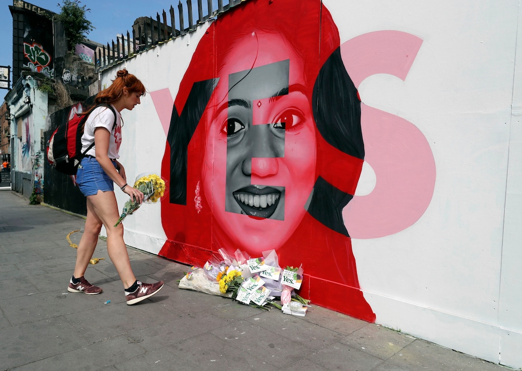 A woman places flowers by a mural showing Savita Halappanavar, a 31-year-old Indian dentist who had sought and been denied an abortion before she died after a miscarriage in a Galway hospital, with the word YES over it, in Dublin, Ireland, on the day of a referendum on the 8th amendment of the constitution. The referendum on whether to repeal the country's strict anti-abortion law is being seen by anti-abortion activists as a last-ditch stand against what they view as a European norm of abortion-on-demand, while for pro-abortion rights advocates, it is a fundamental moment for declaring an Irish woman's right to choose.  (Niall Carson/PA via AP)
