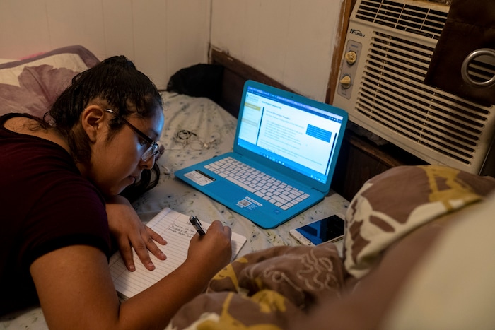 (Ilana Panich-Linsman | The New York Times) Norma Rodriguez, who works two jobs and completes her community college registration by an air conditioner in her family's trailer in Houston, July 20, 2020. Houston, one of America's fastest-warming cities, could average 109 days a year with the heat index topping 100 degrees.
