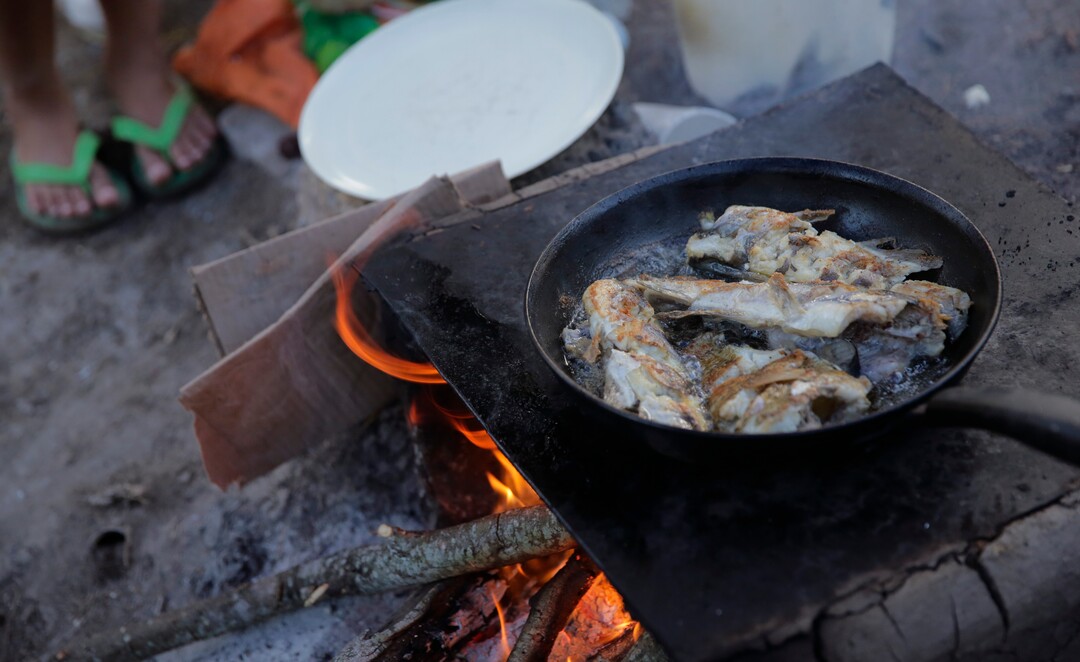 In this Tuesday, Nov. 5, 2019, photo, fish caught in the Rio Grande are cooked in a refugee camp in Matamoros, Mexico. People regularly line up for a half-hour to fill up milk jugs and buckets with water. Some people bathe and wash their clothes in the Rio Grande, known to be contaminated with E. coli and other bacteria. They rely on donors who bring meals or pull fish from the river and fry them over wood fires at the camp. (AP Photo/Eric Gay)