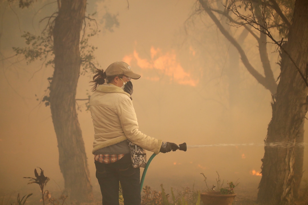 (Marcio Jose Sanchez | AP) Beth Rivera hoses down her property as the Easy fire approaches Wednesday, Oct. 30, 2019, in Simi Valley, Calif. Driven by powerful Santa Ana winds, the brush fire broke out before dawn between the cities of Simi Valley and Moorpark north of Los Angeles and exploded to more than 1,300 acres (526 hectares), threatening 6,500 homes, Ventura County officials said.