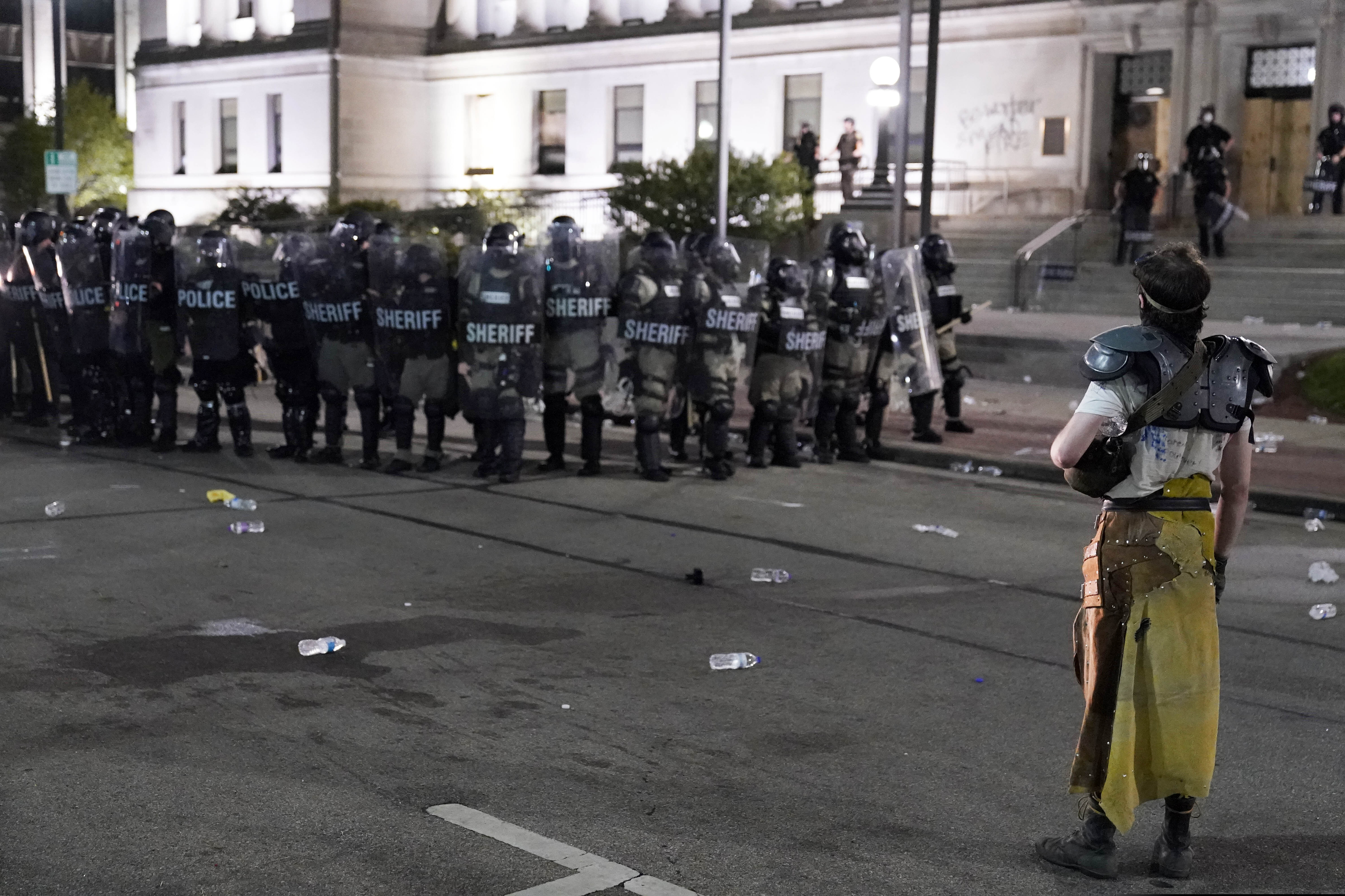 (David Goldman | AP fil ephoto)  A protester stands off with police in riot gear outside the Kenosha County Courthouse, late Monday, Aug. 24, 2020, in Kenosha, Wis.