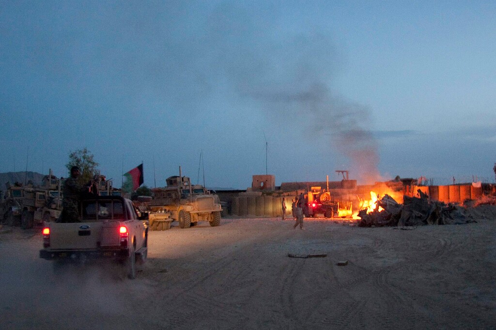 (Simon Klingert | AP) An Afghan National Army pickup truck passes parked U.S. armored military vehicles, as smoke rises from a fire in a trash burn pit at Forward Operating Base Caferetta Nawzad, Helmand province south of Kabul, Afghanistan, April 28, 2011.