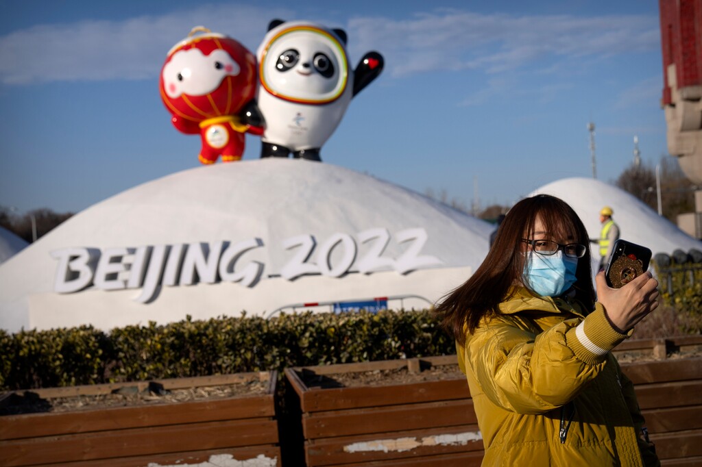 (Mark Schiefelbein | AP) A woman wearing a face mask to protect against coronavirus poses for a selfie with a display of the Winter Paralympic mascot Shuey Rhon Rhon, left, and Winter Olympic mascot Bing Dwen Dwen near the Olympic Green in Beijing, Wednesday, Jan. 12, 2022.