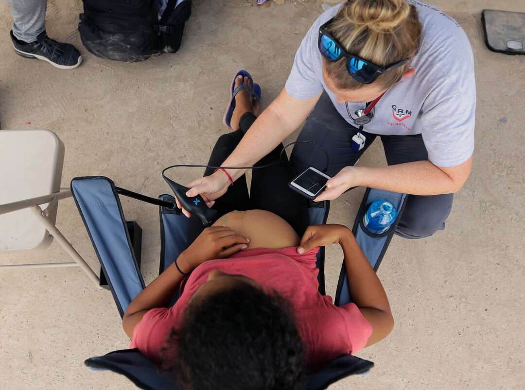 In this Tuesday, Nov. 5, 2019, photo, Helen Perry, top, a nurse practitioner who serves as Global Response Management's operations director, attends to a migrant at a sidewalk clinic in a refugee camp in Matamoros, Mexico. The few doctors and nurses working in the camp are treating people including pregnant women and children with respiratory problems, skin conditions, diarrhea, and other diseases that can be linked to the camp’s unsanitary conditions. (AP Photo/Eric Gay)