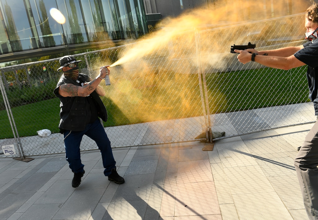 (Helen H. Richardson | The Denver Post via AP) A man sprays mace, left, as another man fatally fires a gun, Saturday, Oct. 10, 2020 in Denver. The man on the left side of the photo was supporting the "Patriot Rally" and sprayed mace at the man on the right side of the image. The man at right, then shot and killed the protester at left. A private security guard working for a TV station was in custody Saturday after a person died from a shooting that took place during dueling protests in downtown Denver, the Denver Post reported.