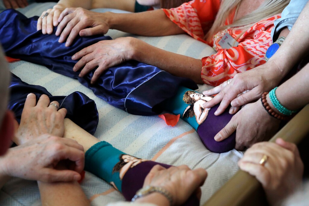 In this May 10, 2019, photo, friends lay their hands on Robert Fuller, wearing angel-themed socks, as he lies unconscious after taking prescribed drugs to end his life, in Seattle. The day he picked to die, Fuller had the party of a lifetime. He's one of about 1,200 people who have used Washington's Death with Dignity Act to end their lives in the decade since it became law. (AP Photo/Elaine Thompson)
