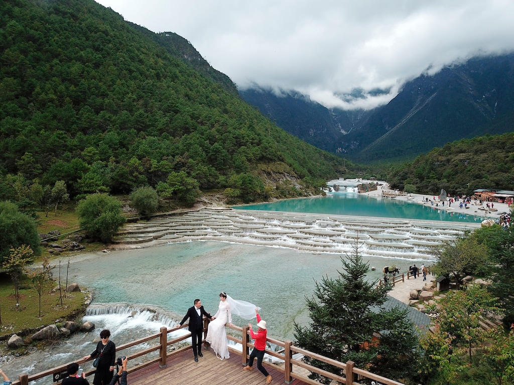 (Sam McNeil | The Associated Press) This Sept. 21, 2018 aerial photo shows a couple posing for photographs at the Valley of the Blue Moon glacial lake fed by the Baishui Glacier No.1 atop the Jade Dragon Snow Mountain in the southern province of Yunnan in China. Scientists say the glacier is one of the fastest melting glaciers in the world due to climate change and its relative proximity to the Equator.