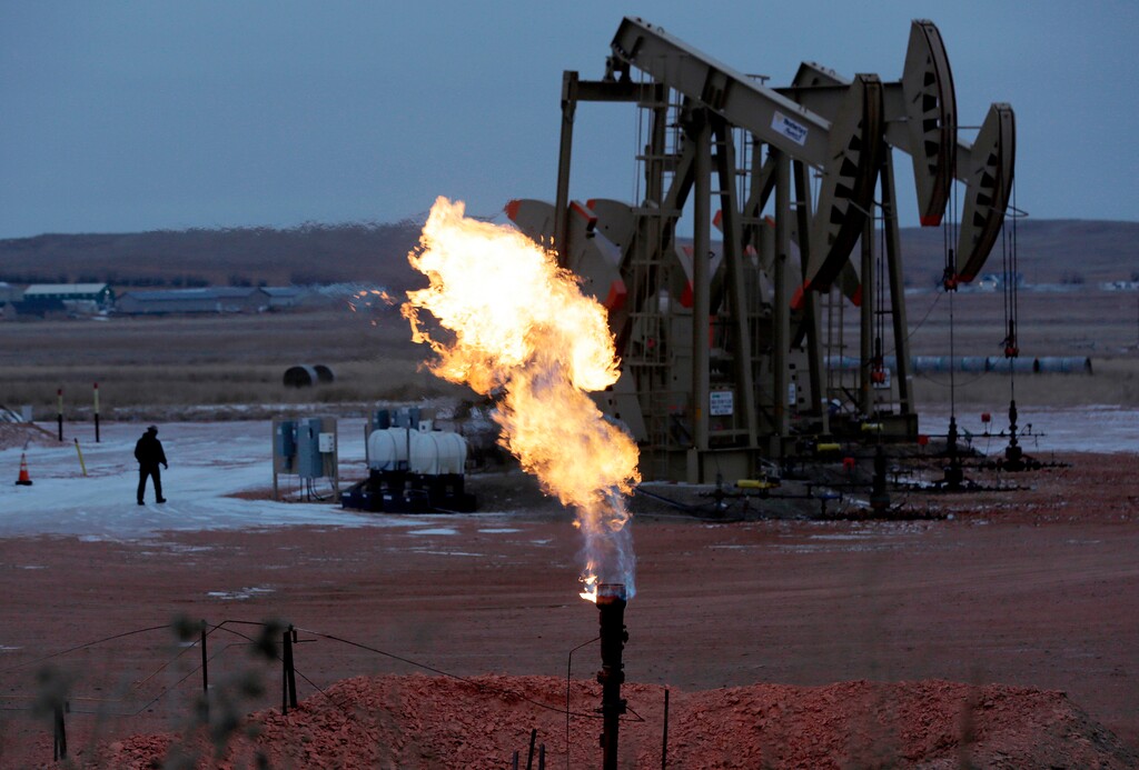 FILE - In this Oct. 22, 2015 file photo, workers tend to oil pump jacks behind a natural gas flare near Watford City, N.D. Natural gas is being burned off and wasted at record levels in North Dakota because development of the pipelines and processing facilities needed to handle it has not kept pace. Natural gas production hit a record in March. But about 20 percent of it went up in flames through “flaring,” the process of burning off the gas when it can’t be captured.  (AP Photo/Eric Gay, File)