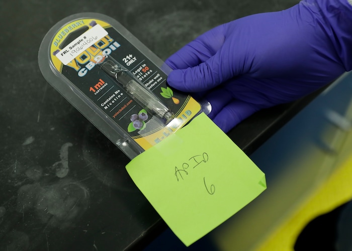 (Ted Warren | AP file photo) A researcher holds a Yolo! brand CBD vape oil cartridge and its packaging at Flora Research Laboratories in Grants Pass, Ore., on July 17, 2019.  Authorities blamed Yolo for sending people to emergency rooms in Utah, saying it contained a dangerous synthetic marijuana. The cartridge pictured here was provided to The Associated Press by a South Carolina man who says he nearly died after puffing it. Testing commissioned by AP shows it contained the same synthetic marijuana that caused the illnesses in Utah.