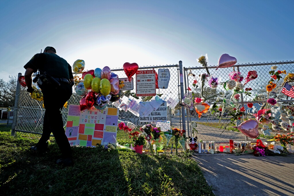 (John McCall/South Florida Sun-Sentinel via AP) A Broward County Sheriff's Office deputy removes police tape from a makeshift memorial at Marjory Stoneman Douglas High School in Parkland, Fla., Sunday, Feb. 18, 2018. Nikolas Cruz, a former student, was charged with 17 counts of premeditated murder on Thursday.