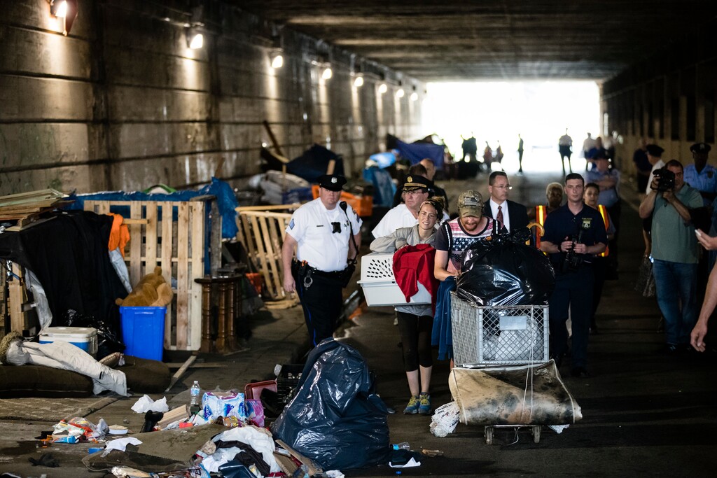 A couple, center, who were living under a bridge carry their possessions out as police move in to clear the encampment in Philadelphia, Wednesday, May 30, 2018.  The city’s homeless packed up their few belongings as sanitation workers cleaned and power washed what had been a heroin encampment only moments before. The morning activity attended by police was part of a month-long pilot program meant to relocate addicts living under two bridges in Philadelphia. (AP Photo/Matt Rourke)