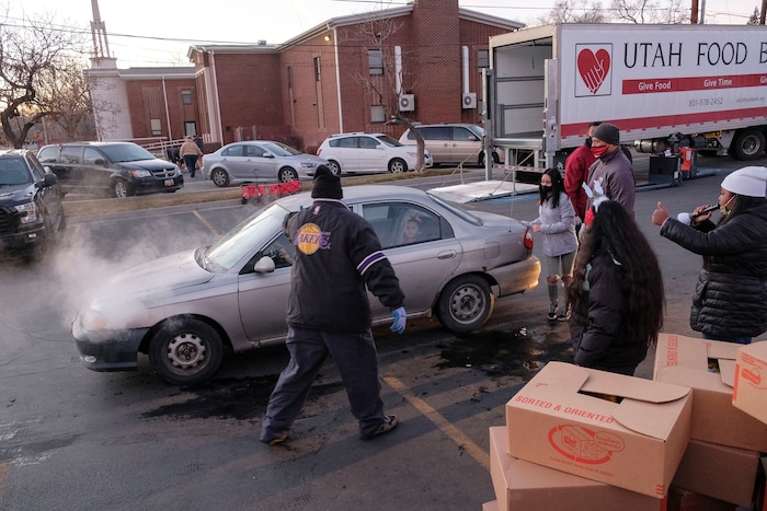 (Leah Hogsten | The Salt Lake Tribune) Volunteer Sam Vatuvei, left, waves an overheating car off after help hand out food from the Utah Food Bank to needy families, Dec. 23, 2020.