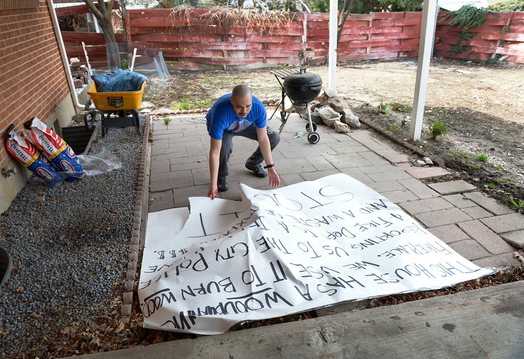(Leah Hogsten  |  The Salt Lake Tribune)  "I wish that someone would've knocked on my door and been honest instead of being passive aggressive," said Nick Smyrniotopoulos of a neighbor's repeated calls to the police and fire department, claiming that Smyrniotopoulos was burning plastics and lighting fires on no-burn days this winter. Smyrniotopoulos jostles with the fallen sign, Wednesday, April 11, 2018, that he and his wife Rebecca hung in front of their house last weekend that reads "This house has a woodburning fireplace. We use it to burn wood. Reporting us to the city, police and fire dept. is a jerk move and a waste of taxpayer $$$. STOP IT."  Smyrniotopoulos said he's never lit a fire on non-burn days and that instead of firewood, he uses Duraflame or Javalog environmentally friendly firelogs.