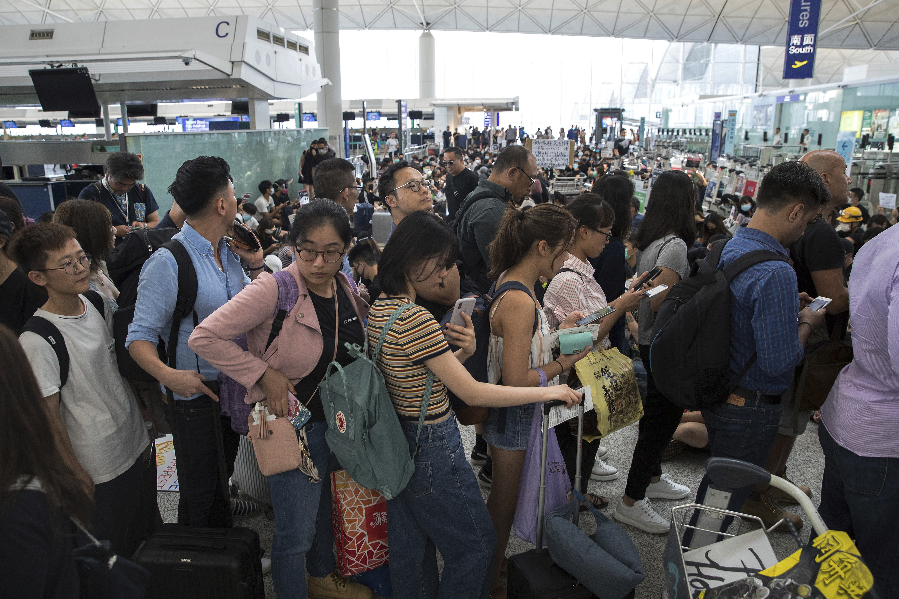 (Vincent Thian | AP Photo) Travelers line up as protesters hold a sit-in rally at the departure gate of the Hong Kong International Airport in Hong Kong, Tuesday, Aug. 13, 2019. Protesters clogged the departure area at Hong Kong's reopened airport Tuesday, a day after they forced one of the world's busiest transport hubs to shut down entirely amid their calls for an independent inquiry into alleged police abuse.