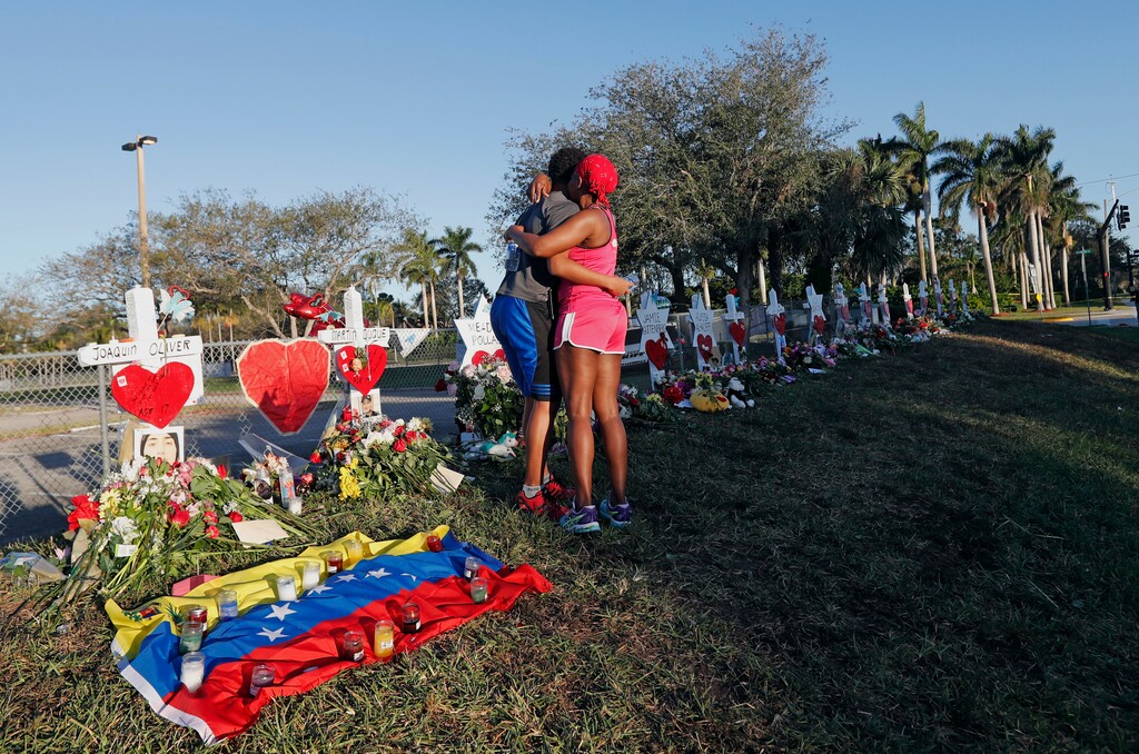 FILE - This Feb. 19, 2018 file photo shows Denyse Christian, hugging her son Adin Christian, 16, a student at the school, at a makeshift memorial outside the Marjory Stoneman Douglas High School, where 17 students and faculty were killed in a mass shooting in Parkland, Fla. Parkland city’s historian Jeff Schwartz is setting a plan in motion to collect, archive and preserve the Marjory Stoneman Douglas mementos. Meanwhile, school administrators have vowed to build a memorial after the demolition of the building where the Feb. 14 attack took place. (AP Photo/Gerald Herbert, File)