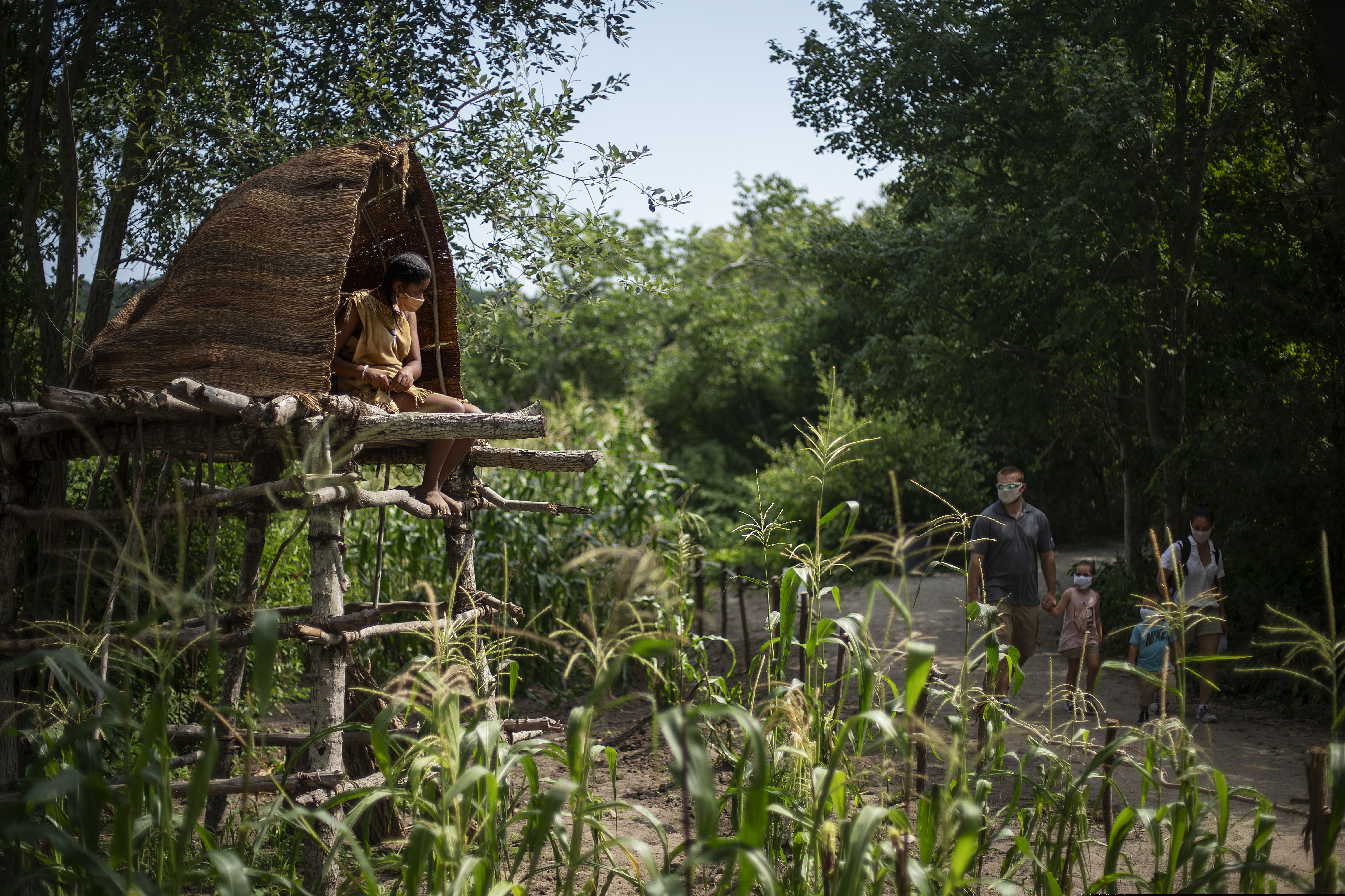 (David Goldman | AP photo)
Alyssa Harris, a member of the Mashpee Wampanoags and a museum educator at Plimoth Plantation, a living history exhibit, sits in a corn watch tower as visitors walk through the Wampanoag Homesite, Wednesday, Aug. 12, 2020, in Plymouth, Mass. A disease outbreak that wiped out large numbers of the Native inhabitants of what is now New England gave the Pilgrims a beachhead in the "New World." So, some historians find it ironic that a pandemic put many of the 400th anniversary commemorations of the Mayflower's landing on hold.