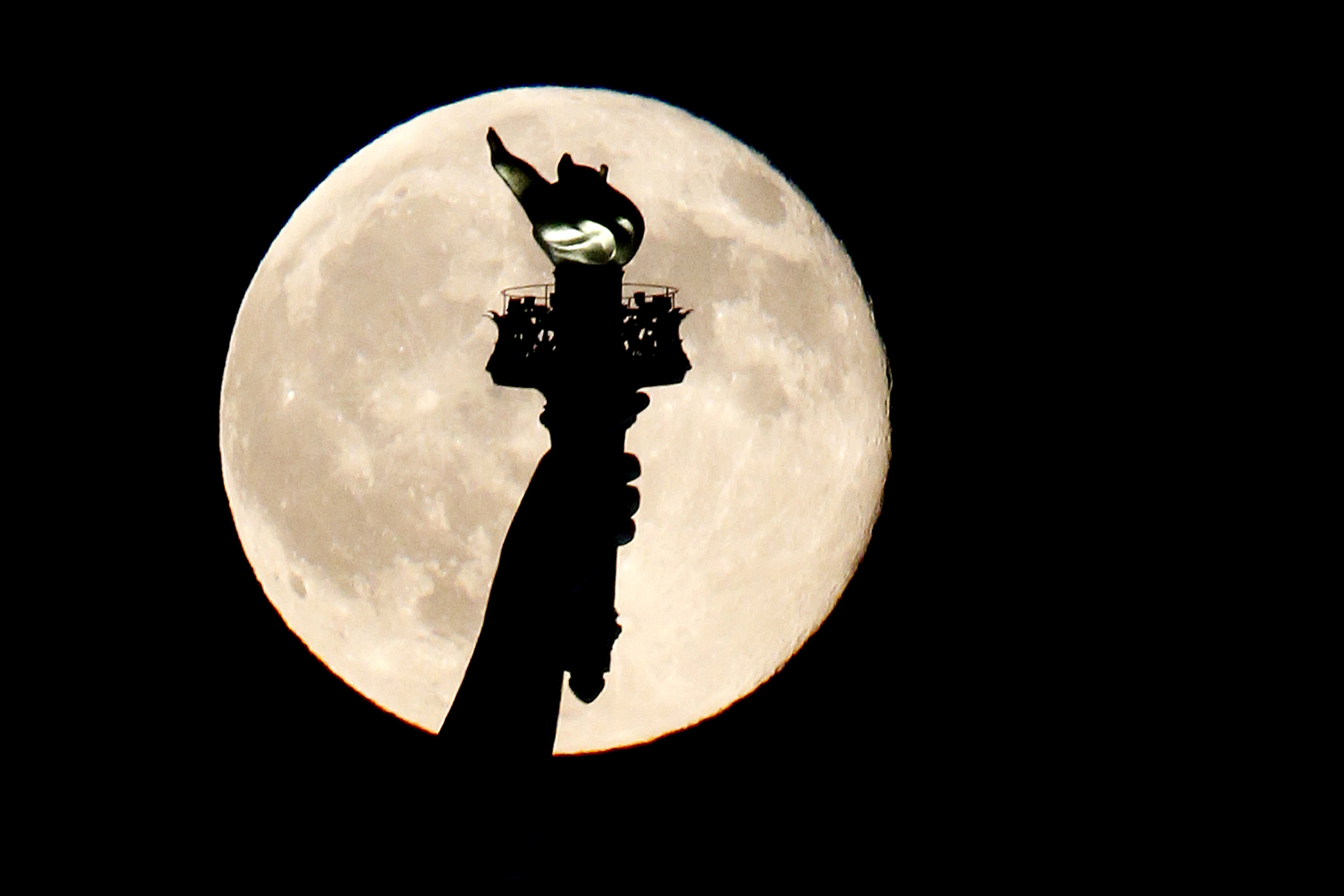 FILE - In this July 31, 2015, file photo, a blue moon rises behind the torch of the Statue of Liberty seen from Liberty State Park in Jersey City, N.J.  (AP Photo/Julio Cortez, File)