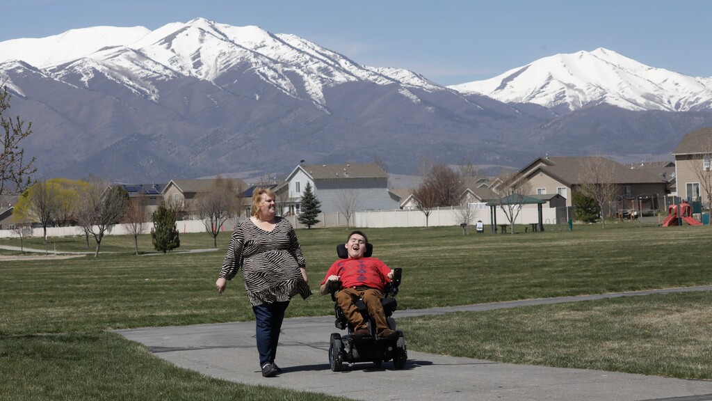(Rick Bowmer | AP) Jodi Hansen walks with her son Jacob Hansen near their home, in Eagle Mountain, April 14, 2020. Even before the new coronavirus hit, cystic fibrosis meant a cold could put Jacob Hansen in the hospital for weeks. He relies on hand sanitizer and disinfecting wipes to keep germs at bay because has cerebral palsy and uses a wheelchair, but these days shelves are often bare. For millions of disabled people and their families, the coronavirus crisis has piled on new difficulties and ramped up those that already existed.