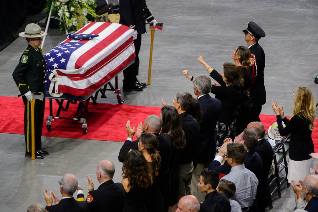 (Trent Nelson | The Salt Lake Tribune)  Fmaily members stand and applaud at the funeral services for Battalion Chief Matthew Burchett at the Maverik Center in West Valley City, Monday Aug. 20, 2018.