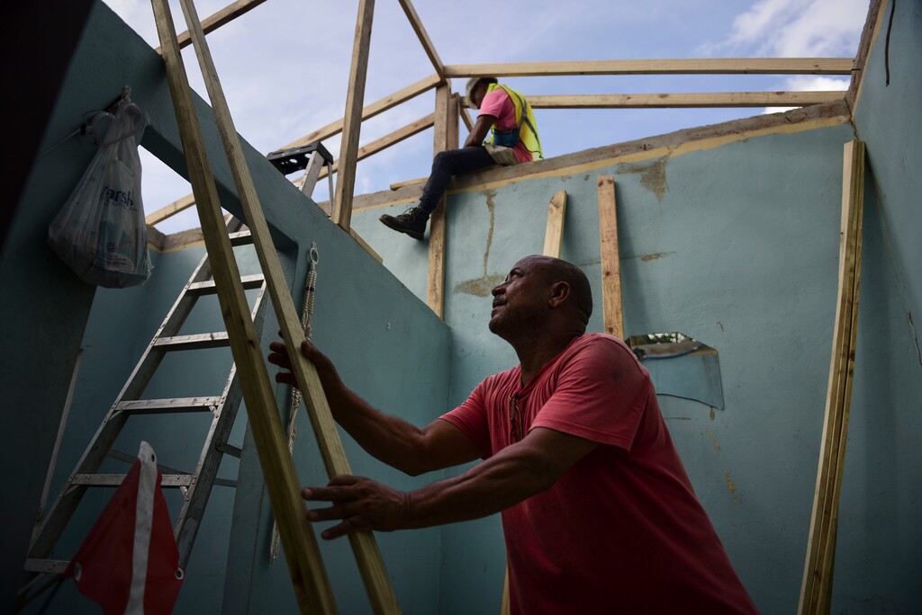 Pedro Deschamps helps workers hired by FEMA to carry out the installation of a temporary awning roof at his house, which suffered damage during Hurricane Maria, in San Juan, Puerto Rico, Wednesday, Nov. 15, 2017. A newly created Florida company with an unproven record won more than $30 million in contracts from the Federal Emergency Management Agency to provide emergency tarps and plastic sheeting for repairs to hurricane victims in Puerto Rico. Bronze Star LLC never delivered those urgently needed supplies, which even months later remain in demand on the island.   (AP Photo/Carlos Giusti)