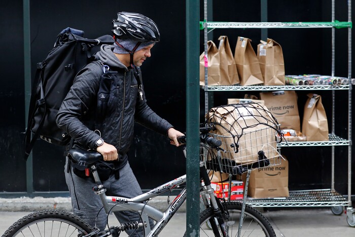 In this Wednesday, Dec. 20, 2017, photo, a bicyclist with a backpack and basket of customer orders prepares to make deliveries for Amazon Prime Now, in New York. (AP Photo/Mark Lennihan)