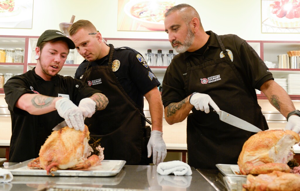 (Leah Hogsten  |  The Salt Lake Tribune) l-r Salt Lake Institute of Culinary Education pastry chef Brixton Taylor helps Sgt. Matt Oehler and Sgt. Joe Cummings carve a turkey. Members of the South Salt Lake Police Athletic League (PAL) joined South Salt Lake Police officers to prepare Thanksgiving dinner kits for families in need in South Salt Lake City, Nov. 26, 2019. 