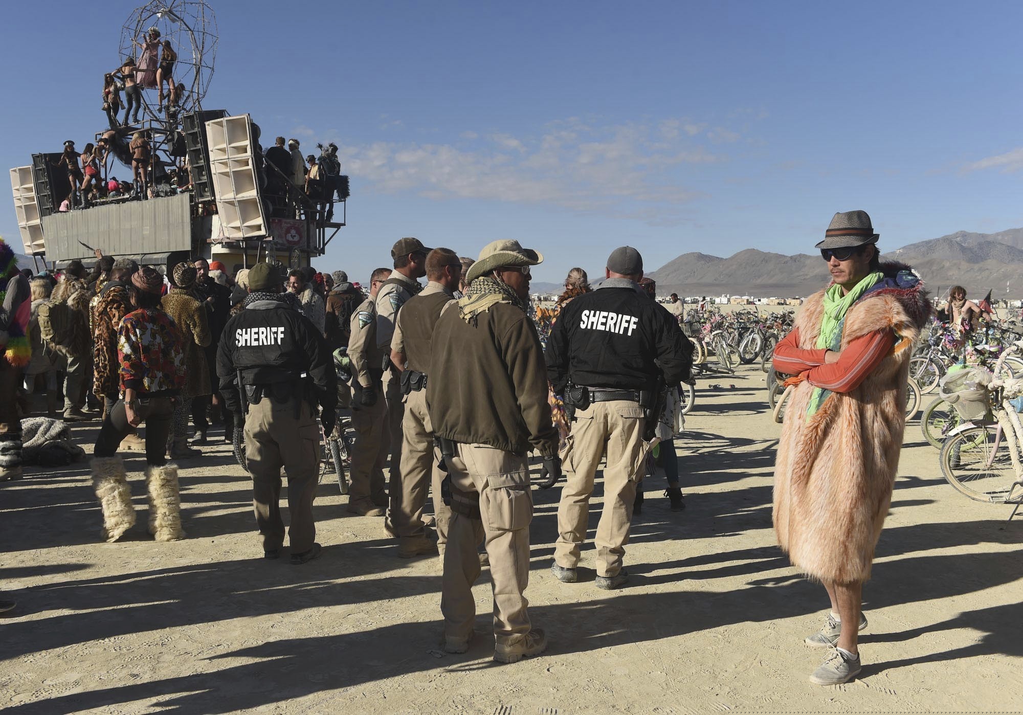 (Andy Barron/Reno Gazette-Journal via AP) In this Sept. 5, 2015 photo, Sheriffs keep an eye on "burners" at a party at Burning Man in the Black Rock Desert near Gerlach, Nev. Burning Man organizers say they won't challenge the U.S. Bureau of Land Management's plans to cap their attendance at current levels under a new 10-year permit but they will fight any move toward federally-sanctioned screenings for weapons and drugs at the counterculture celebration. BLM proposed earlier this month that private security firm be hired to screen all vehicles and participants. Burning Man says it would subject "a peaceable gathering of people to searches without probable cause."