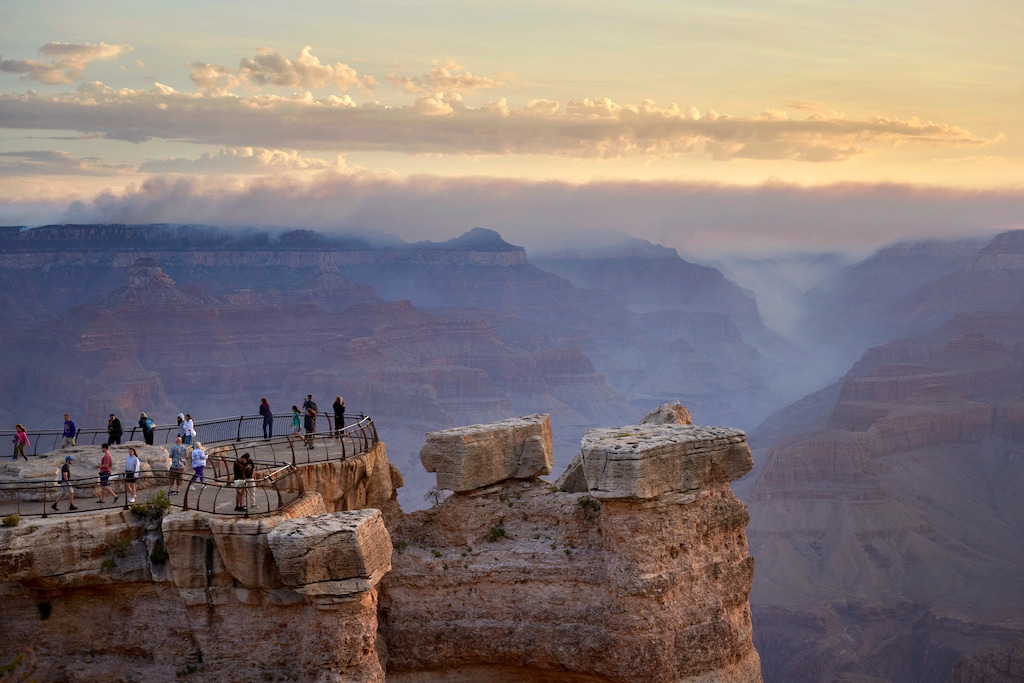 (Bridget Bennett | The New York Times) Visitors gather at Mather Point on the South Rim as smoke from the Dragon Bravo Fire on the North Rim rises at sunrise, in Grand Canyon Village, Ariz., July 15, 2025. Residents, along with Arizona’s political leaders, are asking why the Dragon Bravo fire, sparked by lightning on July 4, was allowed to burn for days in hot, dry conditions before it exploded beyond fire containment lines and tore through the heart of the North Rim.