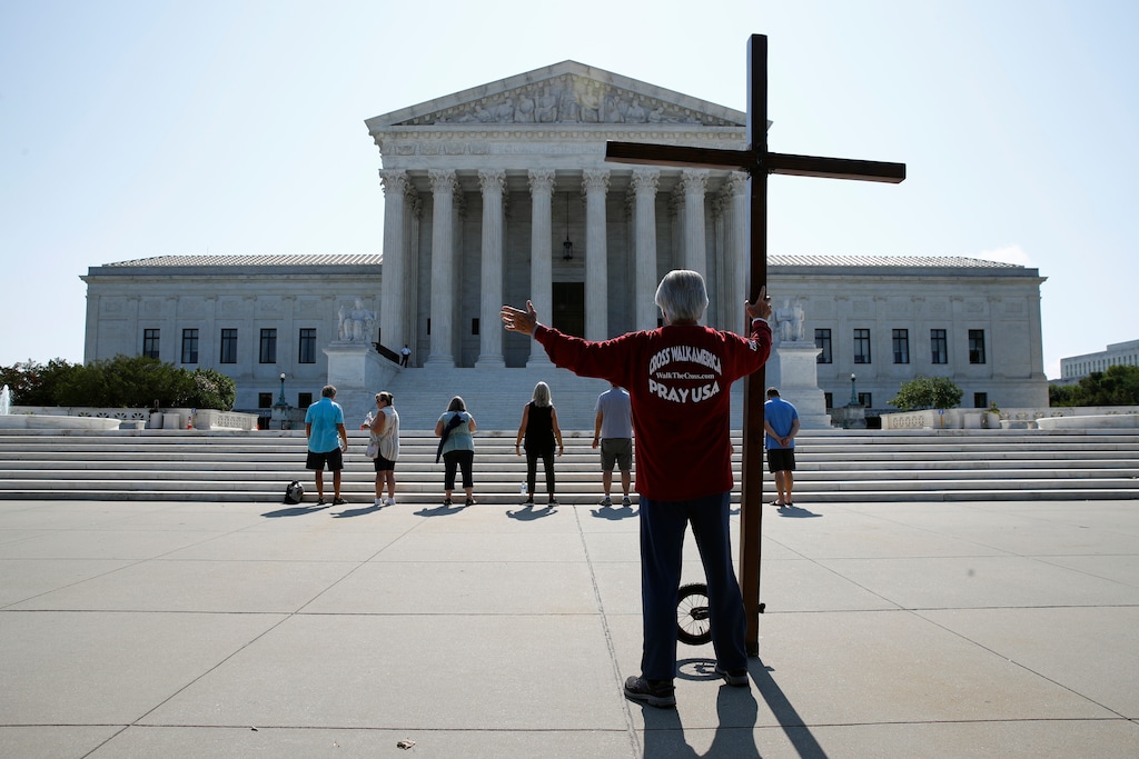 (Patrick Semansky | AP) Tom Alexander holds a cross as he prays prior to rulings outside the Supreme Court on Capitol Hill in Washington, Wednesday, July 8, 2020. The Supreme Court is siding with two Catholic schools in a ruling that underscores that certain employees of religious schools, hospitals and social service centers can’t sue for employment discrimination.