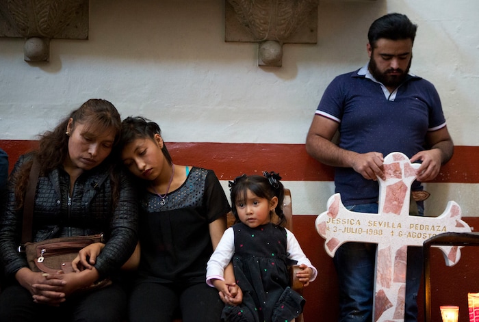 In this Aug. 18, 2017 photo, family members of slain Dr. Jessica Sevilla Pedraza attend a church service, holding a cross for her grave which they brought to be blessed with holy water, in Villa Cuauhtemoc, Mexico state. The daughter of a truck driver and a shop owner, Jessica went to college and became a doctor, cementing her place as the pride of the family. Jessica's mother Juana and sister Ingrid comfort each other as ex-partner Alejandro Colin Garcia holds the cross. (AP Photo/Rebecca Blackwell)