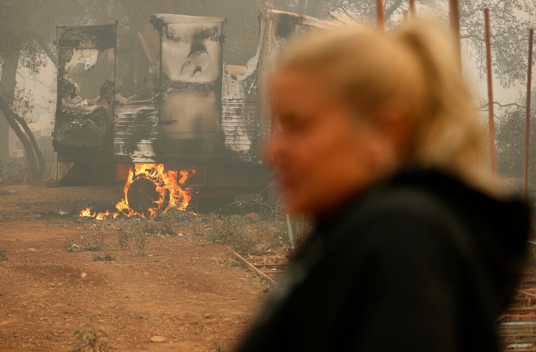 A vehicle burns near the home of Krystin Harvey, right, Saturday, Nov. 10, 2018, in Paradise, Calif. Harvey lost her home in the Camp Fire. (AP Photo/John Locher)