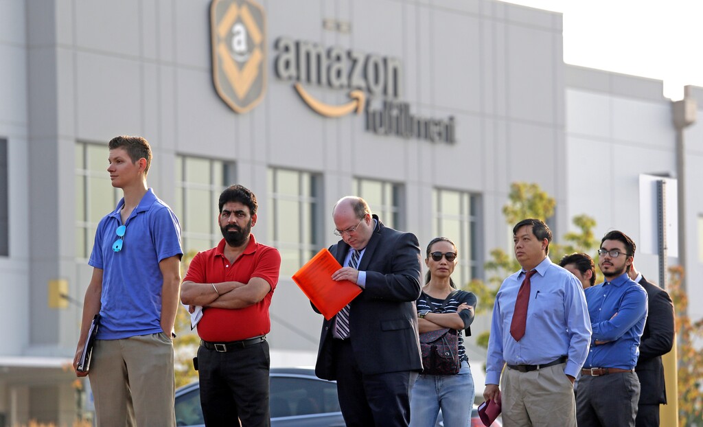 FILE - In this Wednesday, Aug. 2, 2017, file photo, applicants wait in line to enter a job fair at an Amazon fulfillment center, in Kent, Wash. Amazon has narrowed its search for a second headquarters city to 20 locations, concentrated mostly in the East and the Midwest. (AP Photo/Elaine Thompson, File)
