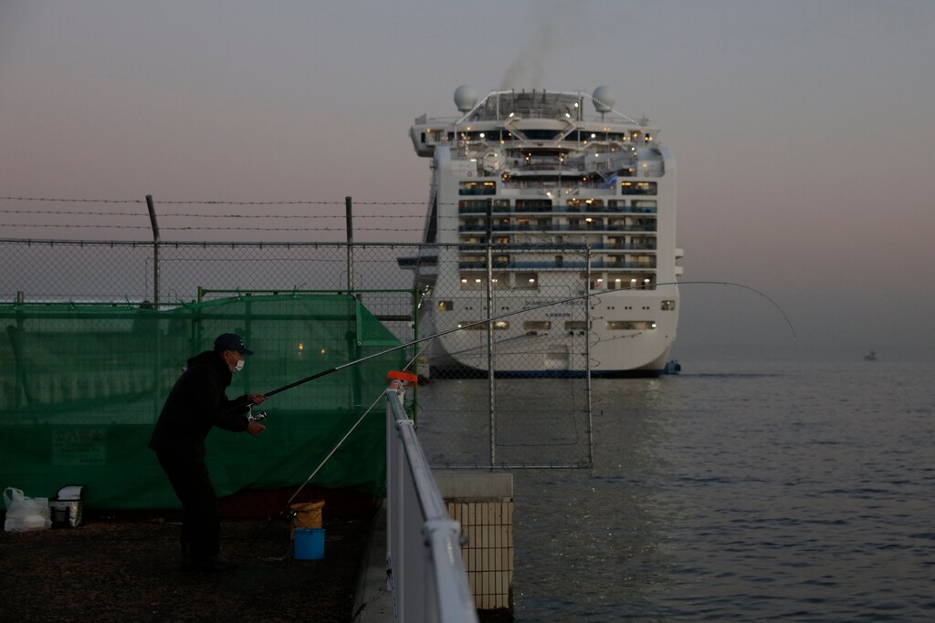 A man fishes behind the quarantined Diamond Princess cruise ship Thursday, Feb. 13, 2020, in Yokohama, near Tokyo. Life on board the luxury cruise ship, which has dozens of cases of a new virus, can include fear, excitement and soul-crushing boredom, according to interviews by The Associated Press with passengers and a stream of tweets and YouTube videos. (AP Photo/Jae C. Hong)
