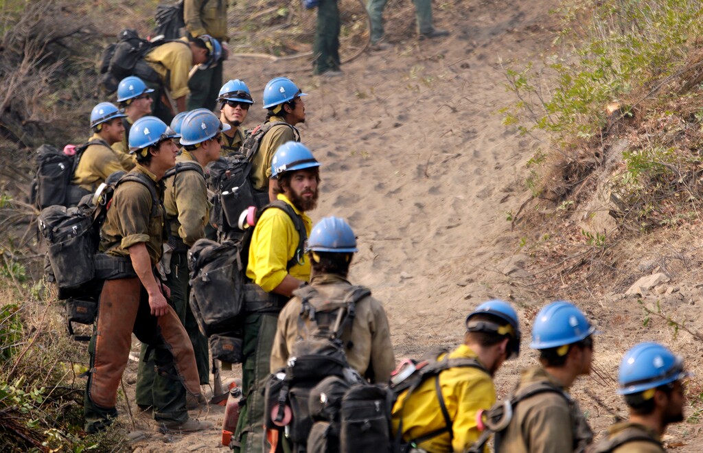 (Elaine S. Thompson | AP file photo) Firefighters from the University of Alaska (Fairbanks) watch as a wildfire slowly creeps toward their fire break near Chelan, Wash., Aug. 27, 2015. Newly released national plans for fighting wildfires during the coronavirus pandemic are hundreds of pages long but don't offer many details on how fire managers will get access to COVID-19 tests or exactly who will decide when a crew needs to enter quarantine.