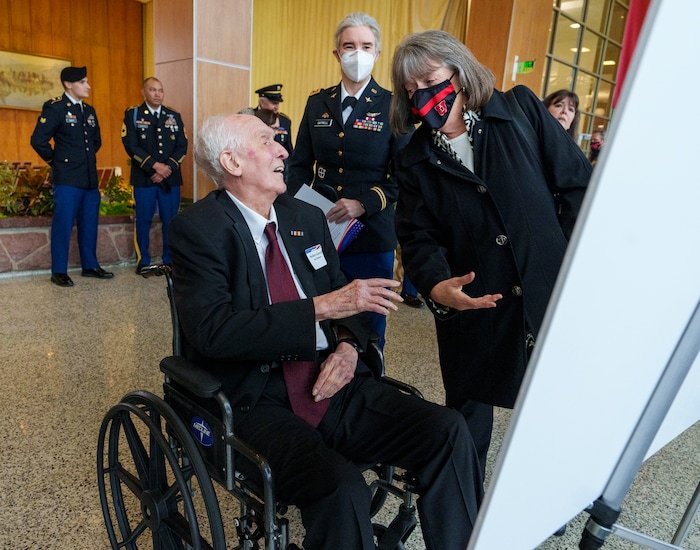 (Leah Hogsten | The Salt Lake Tribune) 2021 Honoree Lt. Col. Wallace B. Gatrell, age 100, with his granddaughter Lt. Col. Deborah Gatrell, center, laughs with an unknown well-wisher after she asked him whether the information on the placard about his life and service in the Army was correct. "I don't know," said Gatrell, "I'm still reading it,"  during the Veterans Day Commemoration ceremony, Nov. 11, 2021 at The University of Utah's Olpin Union Building. Eleven Utah veterans were honored during the 24th Annual Commemoration Ceremony that included bagpipe procession, medallion presentation, and cannon salute.