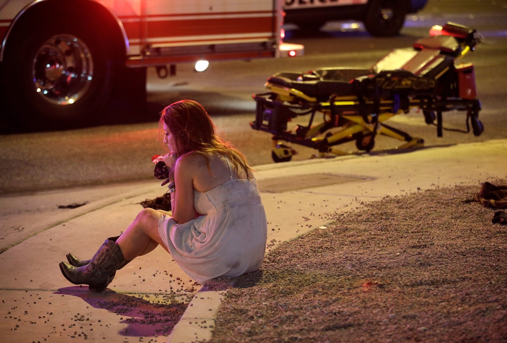 A woman sits on a curb at the scene of a shooting outside of a music festival along the Las Vegas Strip, Monday, Oct. 2, 2017, in Las Vegas. Multiple victims were being transported to hospitals after a shooting late Sunday at a music festival on the Las Vegas Strip. (AP Photo/John Locher)
