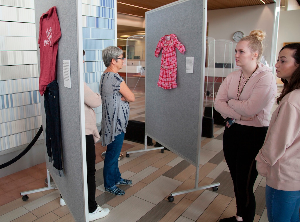 (Chris Caldwell/The Spectrum via AP) In this April 2, 2018, photo, representatives from the Dove Center and the DSU Women's Resource Center display clothes worn by sexual assault victims in a project titled "What Were You Wearing?" The new exhibit at Dixie State University showcases the clothes sexual abuse victims were wearing at the time of their assaults to dispel the myth that a person’s clothing justifies or condones the acts of sexual violence.