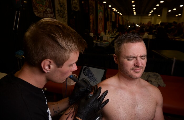 (Leah Hogsten | The Salt Lake Tribune) Adam Hiatt winces as Salt Lake Tattoo Co. artist Landon Barney puts the final touches on his nautilus tattoo at the Salt Lake City International Tattoo Convention, Saturday, March 17, 2018. "Go big or go home," said Hiatt, 33, of his first tattoo, shown in a drawing in the background. Hiatt and his brother came to the show Saturday to get their first tattoos.