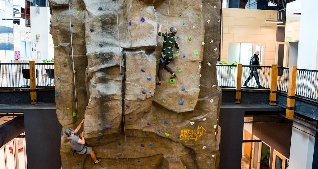 Leah Hogsten | The Salt Lake Tribune Recursion Pharmaceuticals employees l-r Tarl McCallson and Katy Van Pelt climb the company's indoor wall, Oct. 31, 2018. The newly remodeled building still has repurposed features of the previous tenant, Dick's Sporting Goods, including the climbing wall that employees conquer when they need a quick, creative break and an open floor plan, where the separation between departments, as well as managers and employees, is blurred. Recursion Pharmaceuticals, a biotechnology company, has opened it's new headquarters in Salt Lake City at The Gateway.