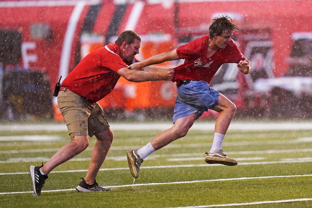 (Rick Bowmer | AP) A spectator, right, is dragged down after he ran onto the field during a rain delay during the first half of an NCAA college football game between Weber State and Utah on Thursday, Sept. 2, 2021, in Salt Lake City.