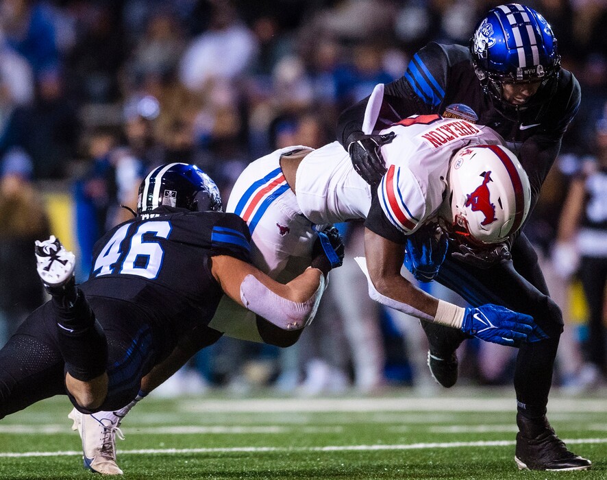 SMU's Camar Wheaton, center, is tackled by BYU's Logan Pili (46) and  Matthew Criddle, right, during the first half of the New Mexico Bowl NCAA college football game in Albuquerque, N.M., Saturday, Dec. 17, 2022. (Chancey Bush/The Albuquerque Journal via AP)