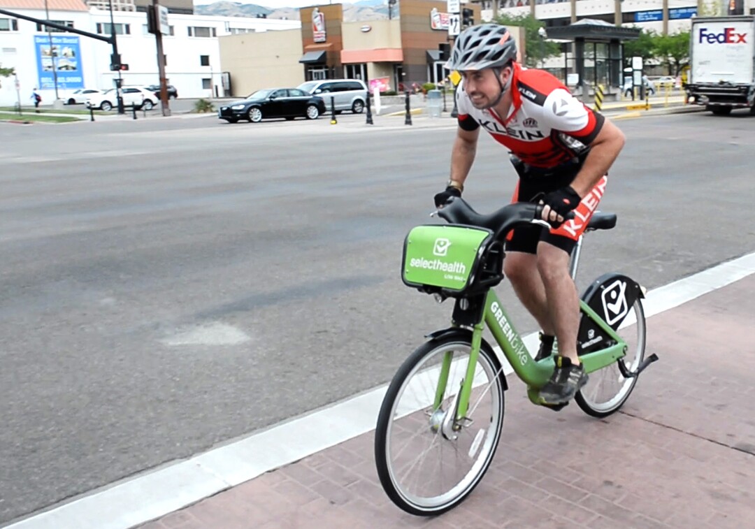 (Rick Egan  |  The Salt Lake Tribune)       Salt Lake Tribune reporter Ben Wood crosses 200 East on his Green Bike at the start of a race against colleagues from Library Square to the Tribune building at the Gateway on Thursday, Aug. 2, 2018. 