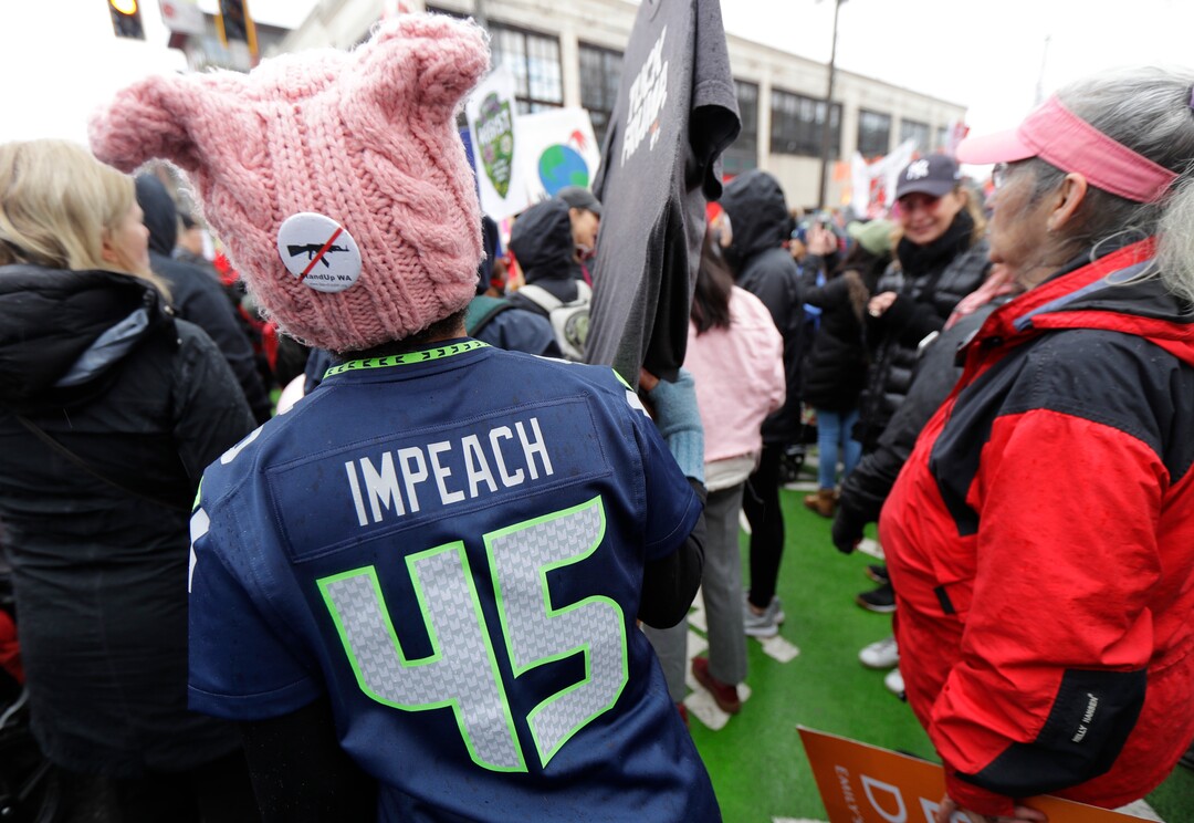 A woman wears a Seattle Seahawks jersey making reference to impeaching President Donald Trump as she takes part in a Women's March in Seattle, Saturday, Jan. 20, 2018. The march was one of dozens planned across the U.S. over the weekend. (AP Photo/Ted S. Warren)