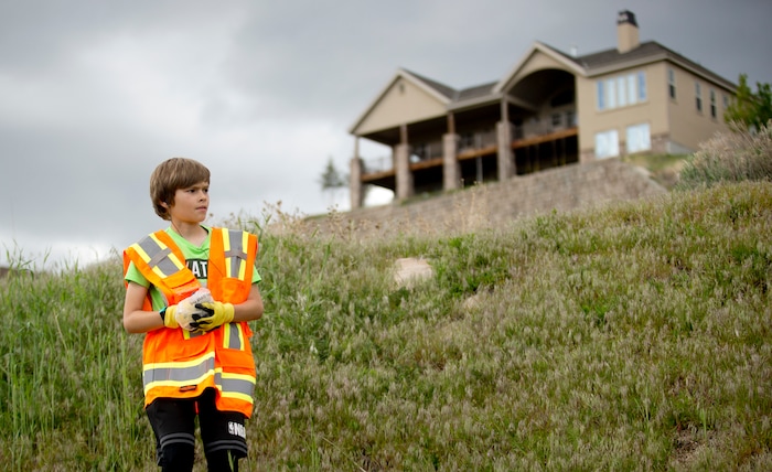 In a Wednesday, May 8, 2019 photo, Damon Haub, 10, of Lehi, gathers up trash as he and other volunteers help to complete an Eagle Scout Service Project that aims to create a walkable path connecting nearby neighborhoods to Ignite Entrepreneurship Academy and a future park, just northwest of the charter school in Lehi, Utah. (Isaac Hale/The Daily Herald via AP)