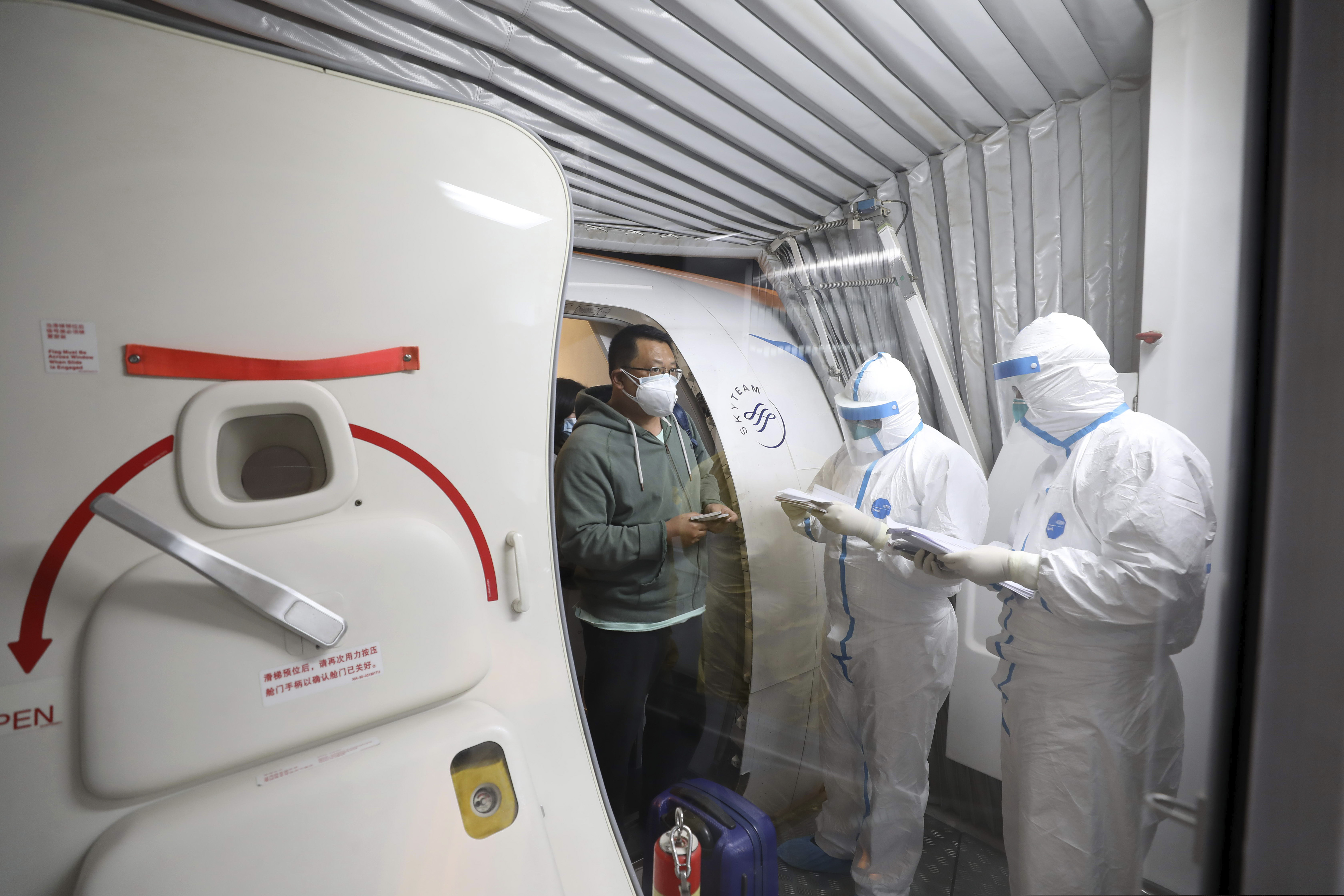(Chinatopix via AP) Quarantine workers in protective suits check identity documents as tourists from the Wuhan area walk off of a chartered plane taking them home from Bangkok at Wuhan Tianhe International Airport in Wuhan in central China's Hubei Province, Friday, Jan. 31, 2020. A group of Chinese tourists who have been trapped in Thailand since Wuhan was locked down due to an outbreak of new virus returned to China on Friday.