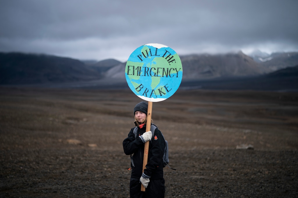 A girl holds a sign that reads 'pull the emergency brake' as she attends a ceremony in the area which once was the Okjokull glacier, in Iceland, Sunday, Aug. 18, 2019. With poetry, moments of silence and political speeches about the urgent need to fight climate change, Icelandic officials, activists and others bade goodbye to the first Icelandic glacier to disappear. (AP Photo/Felipe Dana)