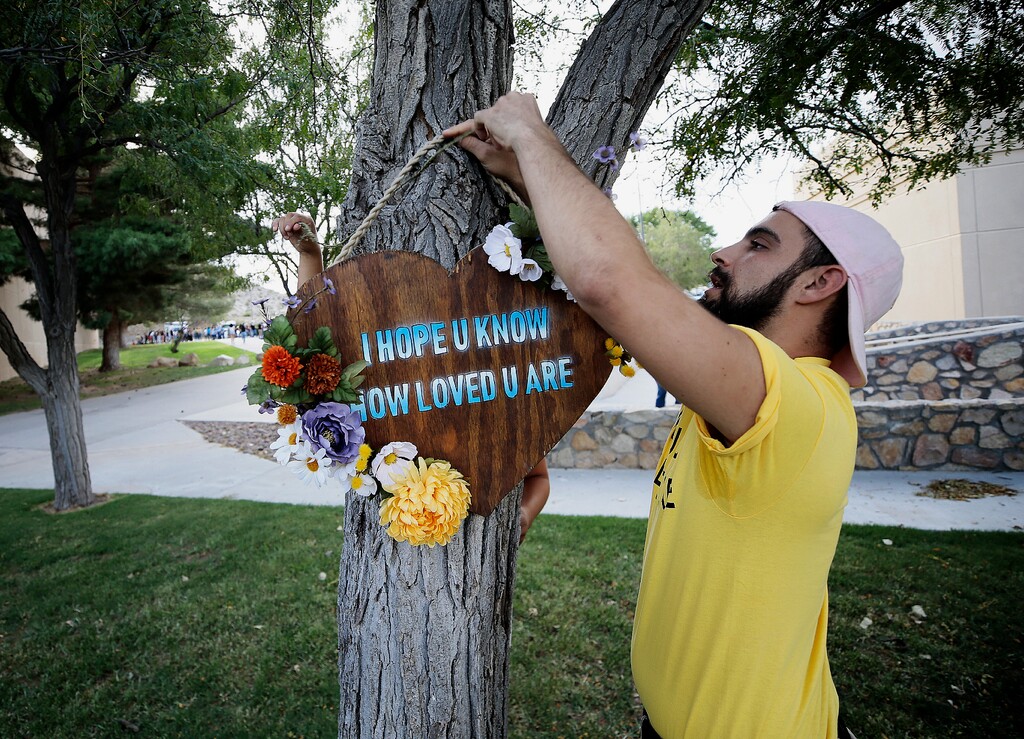 Los Angeles-based artists Noah Reich, right, and David Maldonado, behind the tree, hang a heart-shaped sign on a tree outside a benefit concert by Khalid for the Walmart shooting victims in El Paso, Texas, Sunday, Sept. 1, 2019. (Mark Lambie/The El Paso Times via AP)
