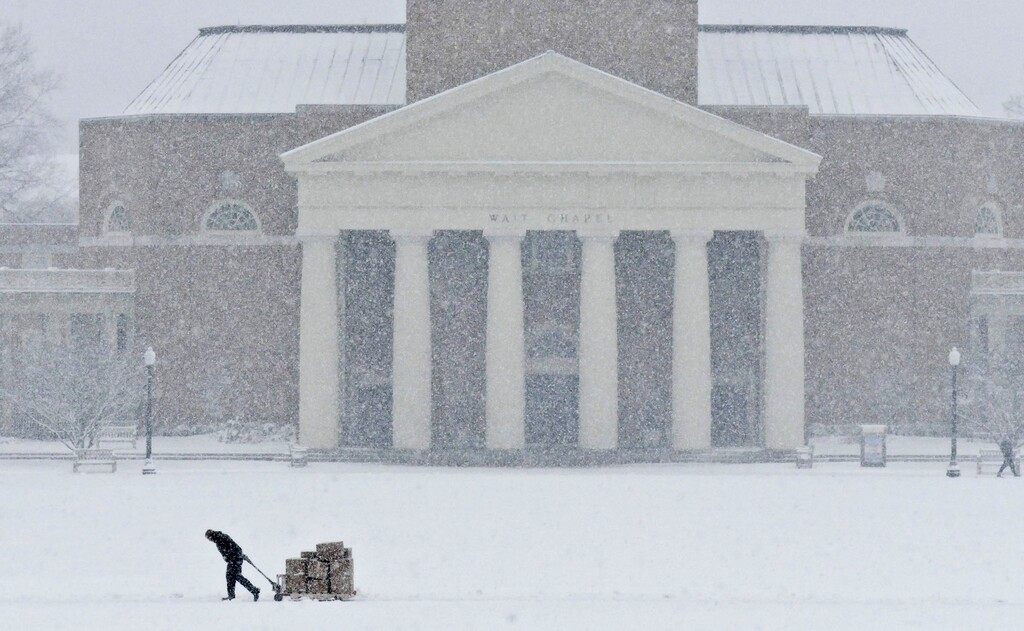 (David Rolfe | The Winston-Salem Journal | The Associated Press) A figure leans into the snow hauling a pallet across the snowy expanse of Hearn Plaza on the Wake Forest University campus in Winston-Salem, N.C., Wednesday, Jan. 17, 2018. The university was closed for the first heavy snowfall of the season.
