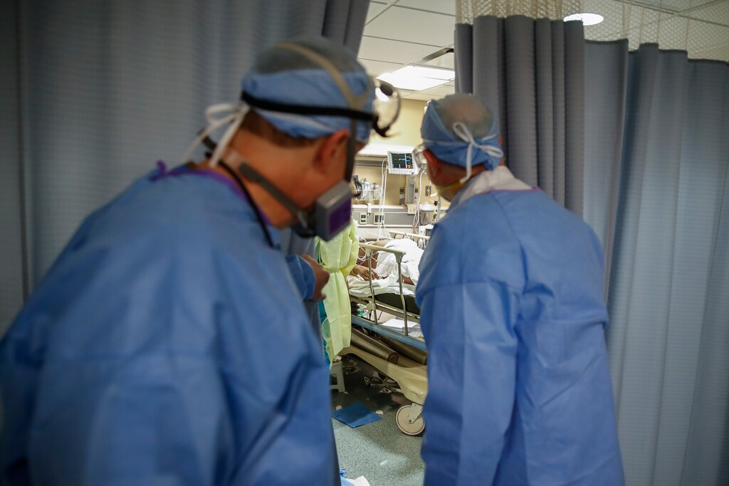 (John Minchillo | AP file photo) Dr. Anthony Leno, Director of Emergency Medicine St. Joseph's Hospital, left, and Dr. James Neuendorf, Director of Medicine, right, look into an exam room where a patient with COVID-19 who went into cardiac arrest was revived, Monday, April 20, 2020, in Yonkers, N.Y.